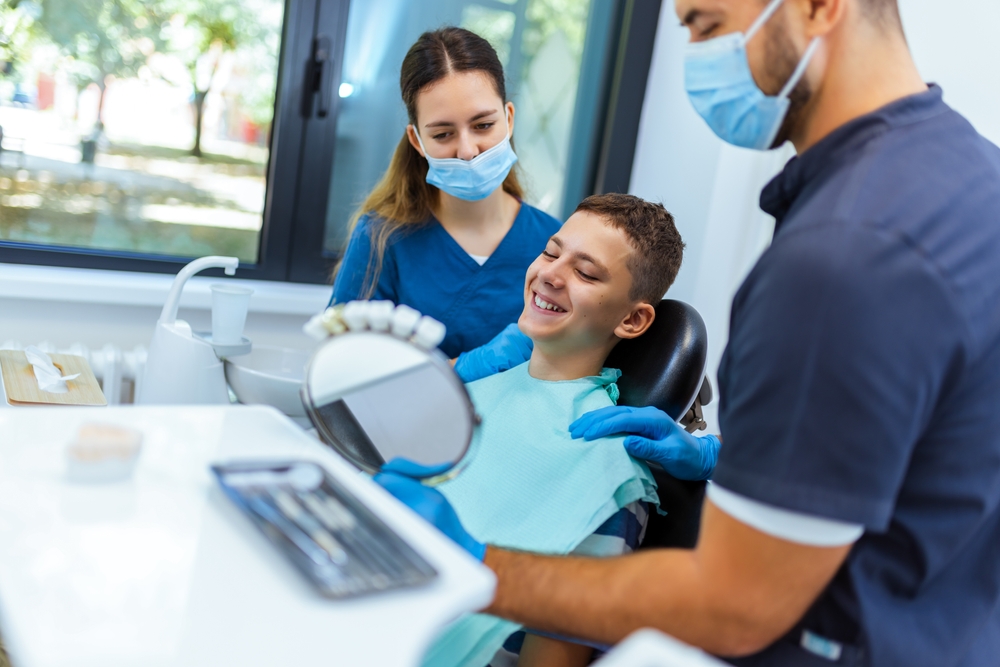 Little,Boy,Sits,In,Dental,Chair,,Smiling,Happily,As,Doctor